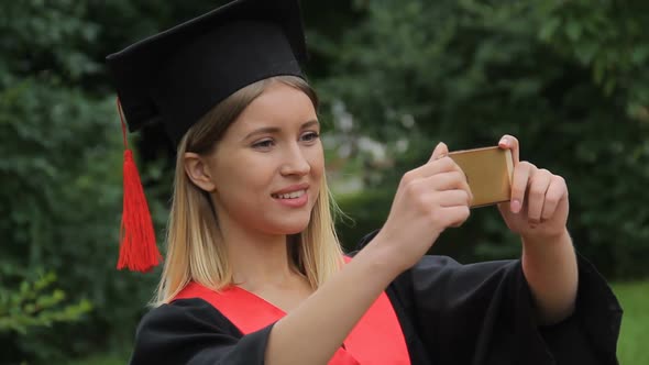 Beautiful Girl in Academic Dress Filming Friends on Smartphone, Happy Graduation