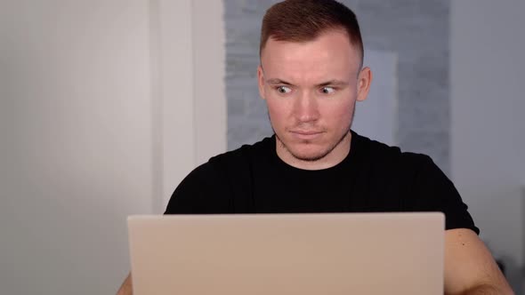 Guy in Tshirt Reads on Laptop Display Stiffening and Blinks