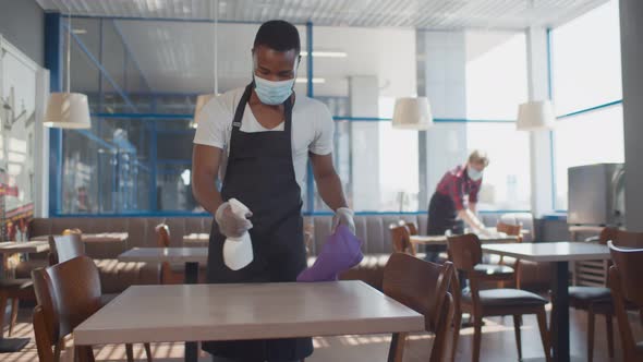 African Male Worker Cleaning Table with Disinfectant in Restaurant During Coronavirus Outbreak