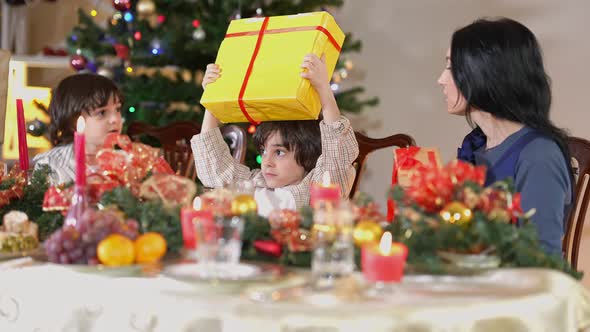 Hyperactive Middle Eastern Boy Shaking Christmas Gift Sitting with Twin Brother and Caucasian Mother