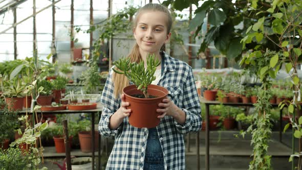 Dolly Shot Slow Motion of Cute Girl Child Walking in Greenhouse Holding Pot Plant Smiling