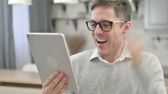 Young Man Celebrating Success on Tablet at Home