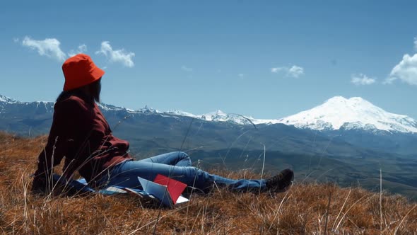 Girl Reads a Book on a Background of Mountains