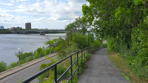 Walking and biking trail with view to street and river below plus bridge and buildings in background