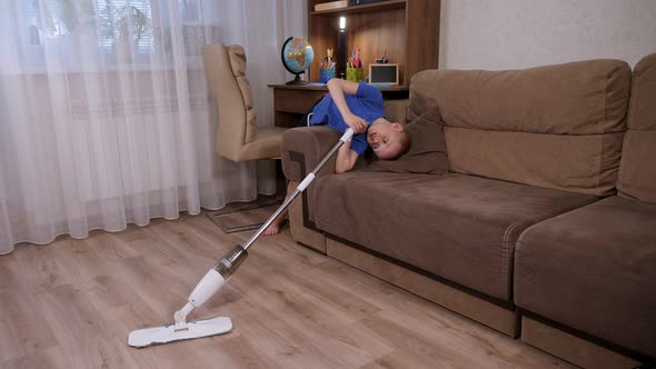 A Little Boy is Mopping the Floor with a Mop and Fooling Around While Cleaning