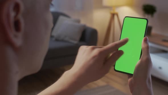 Back View of Man at Living Room at Night Using Phone With Green Mockup Screen Chroma Key Without