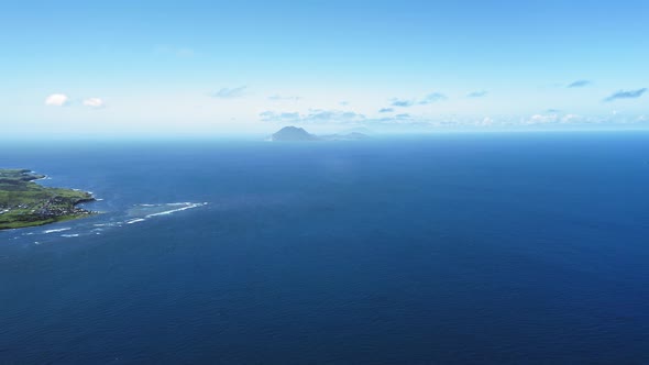 Aerial shot of blue sea, an island with a settlement and shadow of mountain in Saint Kitts and Nevis