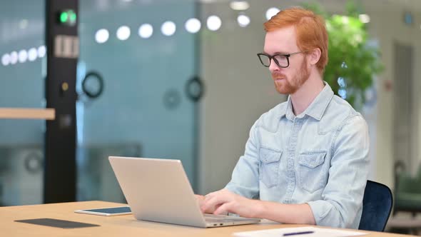 Tired Casual Redhead Man with Laptop Having Neck Pain in Office 