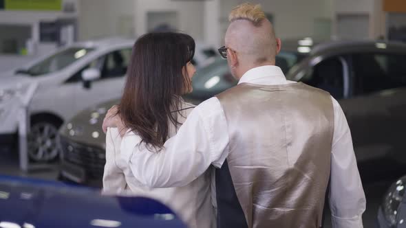 Back View of Husband and Wife Hugging Discussing Car Purchase in Dealership in Slow Motion