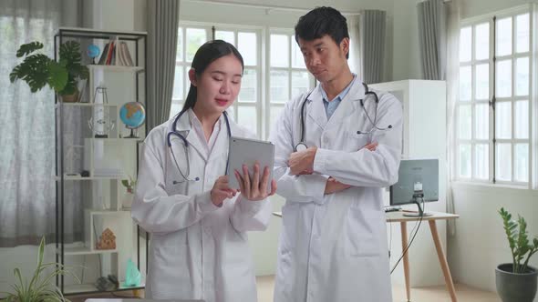 Doctor's Office: Asian Physician Talks With Professional Nurse, Using Tablet Computer