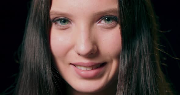 Closeup on the Face of a Brunette Model Smiling at the Camera Against a Black Studio Background