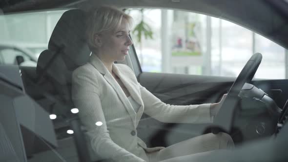 Portrait of Adult Caucasian Businesswoman in Elegant White Suit Sitting on Driver's Seat in Car