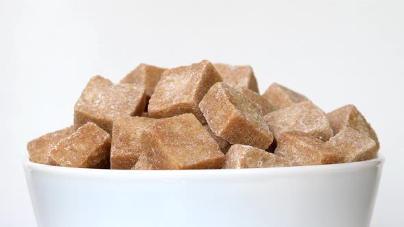 Unrefined sugar pieces in bowl rotating close-up on white background