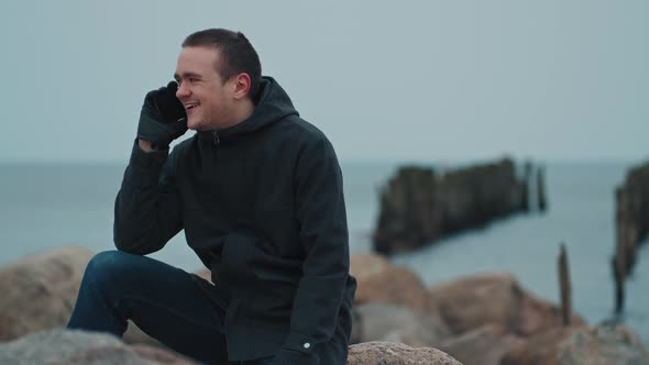 A young guy is sitting on a stone against the background of the blue sea