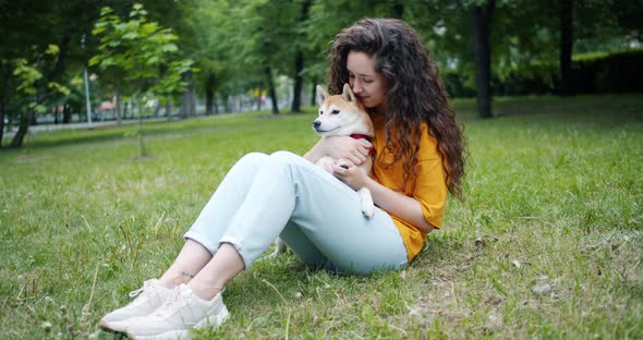 Attractive Brunette Stroking Beautiful Shiba Inu Dog Sitting on Grass in Park