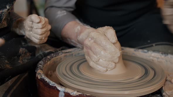 Close-up of Adult and Child's Dirty Hands Molding Clay Into Ceramic Pot on Throwing Wheel