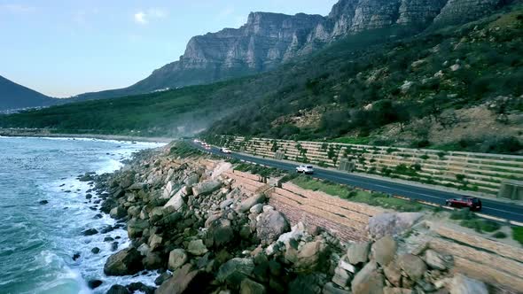 rough and rocky coastline near Camps Bay with cars driving on the coastal highway. aerial wide drone