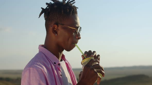 Satisfied Africanamerican Drinks Cocktail Smiles and Dances Against the Background of Field