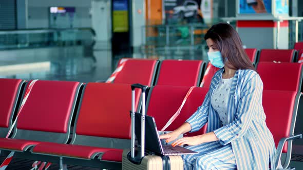 Woman in Protective Mask, with Luggage, Working on Laptop at Airport, While Waiting for Boarding