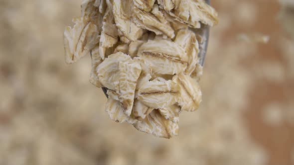 Raw oatmeal flakes fall into a metal spoon in slow motion