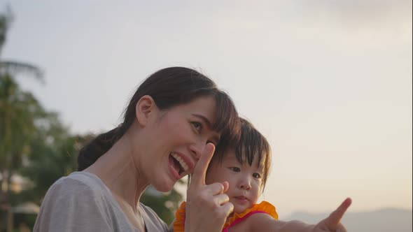 Asian happy mother standing on the beach and holding her baby girl in arm during holiday summer.