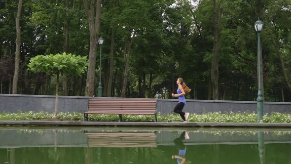 Woman Running Near Pond in Park