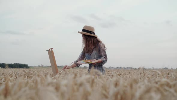 Elegant Lady Painting on Canvas Among Spacious Ripe Wheat Field with Bright Sky