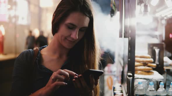 Beautiful Local European Businesswoman Using Smartphone Messenger App Near a Steaming Street Food