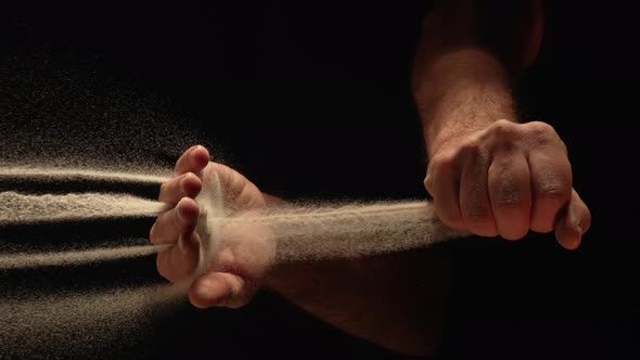 Stream of Dry Sand Pours Into Palm of Man and is Spilling Through His Fingers on Black Background