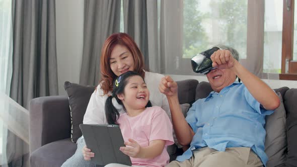 Asian grandparents and granddaughter using virtual reality and tablet play games at home.