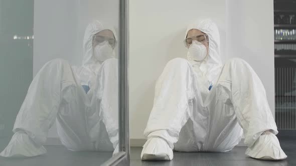 Exhausted Woman in Antiviral Suit and Respirator Sleeping in Gym or Office After Disinfection