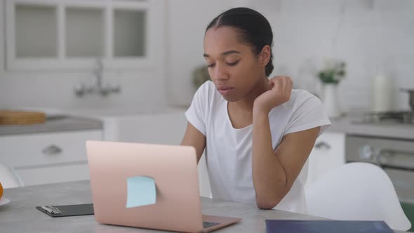 Young Smart Concentrated Woman Sitting at Kitchen Table Typing on Laptop Keyboard Surfing Internet