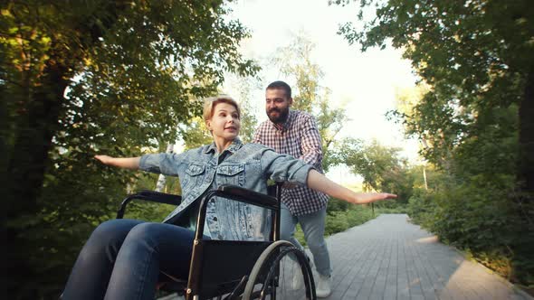 Happy Man Rolls Emotional Disabled Woman in Wheelchair Who Spread Her Arms Like Wings Through Park