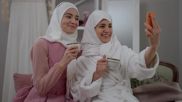 Laughing Happy Muslim Bride and Bridesmaid Talking at Smartphone Streaming in Social Media on