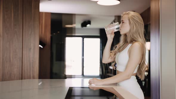 Young Blonde Drinks Water From a Glass and Leans on the Table