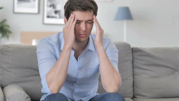 Handsome Young Man with Headache Sitting Tense on Couch