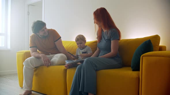 Family Sitting on Yellow Couch and the Baby Drawing Something in a Book