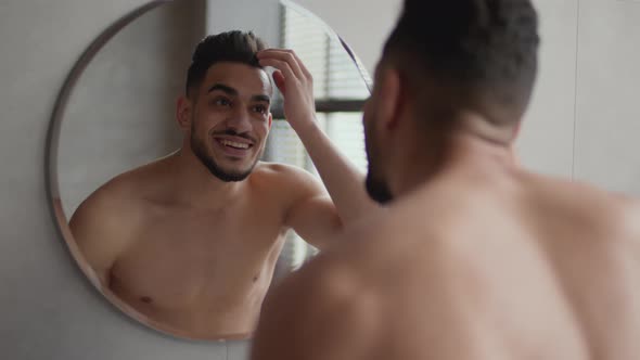 Young Positive Stylish Arabic Guy Styling His Hair Looking at Mirror at Bathroom Fixing His