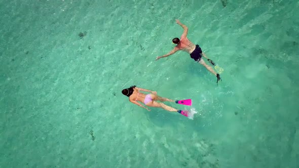 Aerial view of man and woman swimming in masks and flippers in turquoise water.