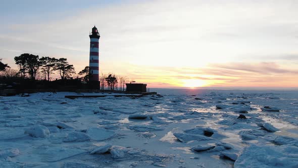 Red and White Lighthouse Stands on Island Against Frozen Sea