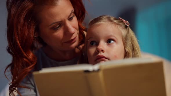 Closeup Portrait of Excited Curios Daughter Listening to Mother Reading Book at Bedtime