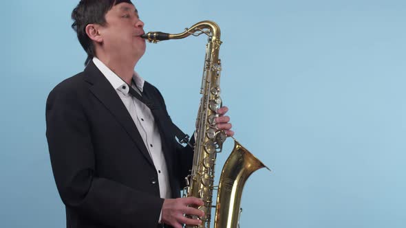 Man Saxophonist Plays the Saxophone in the Studio on a Blue Background and in Dark Light