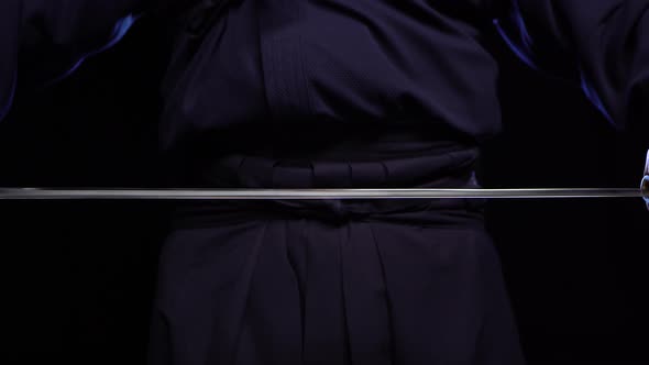 A Close-up Shot of a Ninja Man's Hand Holding a Sword and Raising It.