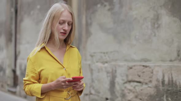 Beautiful Blond Woman Looking and Touching Phone Screen While Walking at Old City Street. Bright