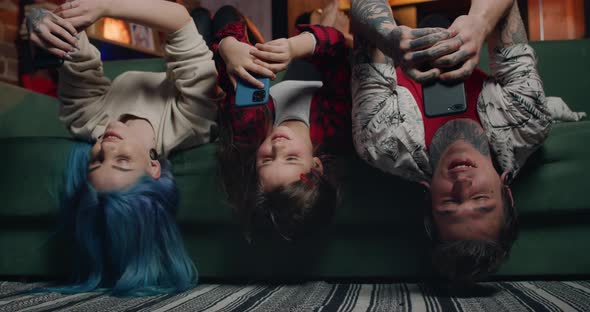 Cheerful Family Lying on Sofa Upside Down and Using Smartphones, Modern Mother, Father and Their Kid