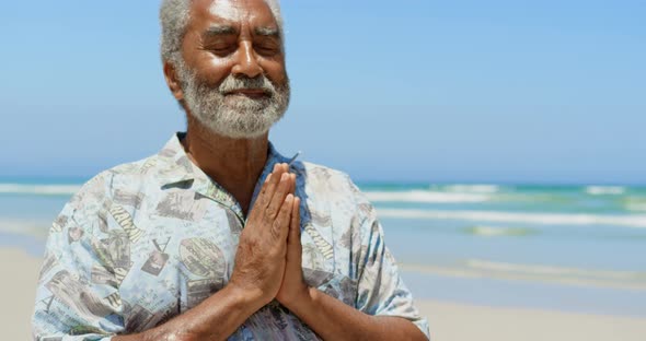 Front view of active senior African American man performing yoga on the beach 4k