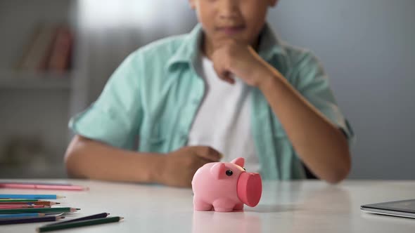 Little Boy Putting Pocket Money in Piggy Bank, Raising Funds for Desired Toy
