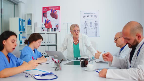 Senior Woman Doctor Standing in Front of Colleagues Presenting Diagnosis