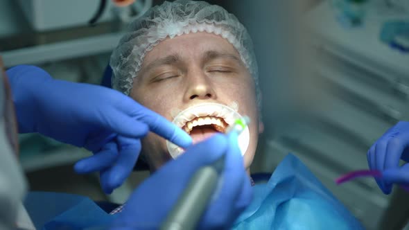 Face of Patient with Closed Eyes in Dental Chair As Doctor and Nurse Appearing with Drill and Saliva