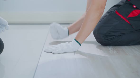 Close-up of Craftsman worker wear gloves, installs laminate board on corridor floor at home.